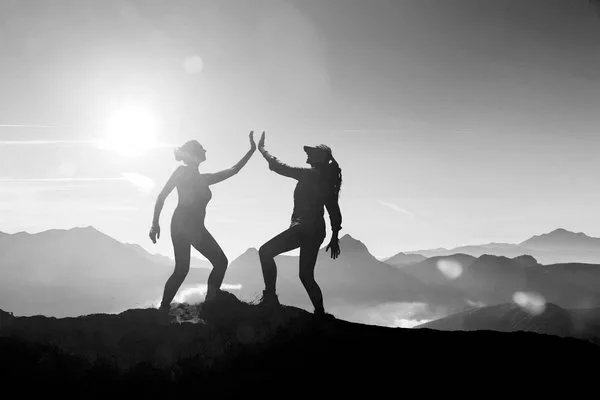 Две женщины дают пять на вершине горы
