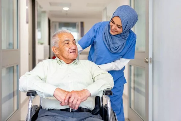 Медсестра-мусульманка ухаживает за пожилым пациентом в инвалидной коляске