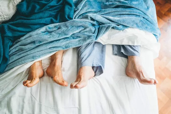 Пожилая пара лежит в постели, их ноги выходят из-под простыней