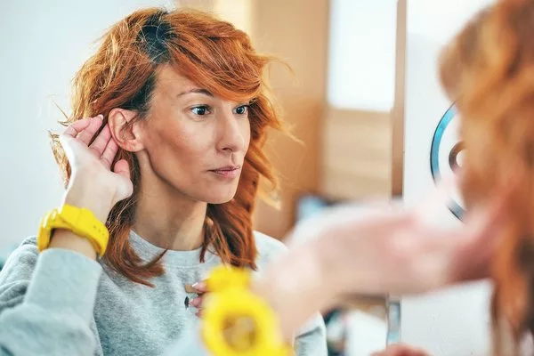 Женщина смотрит в зеркало на ухо