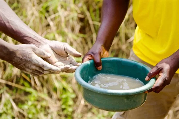 Руки африканских мужчин держат ведро с грязной водой, которая будет использоваться в качестве питьевой