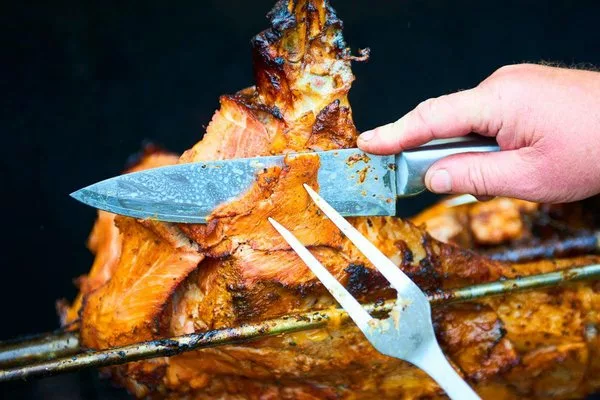 Руки шеф-повара режут ножом целую жареную свинину на стейки