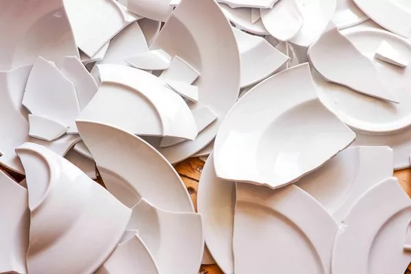 Много белых разбитых тарелок на деревянном полу